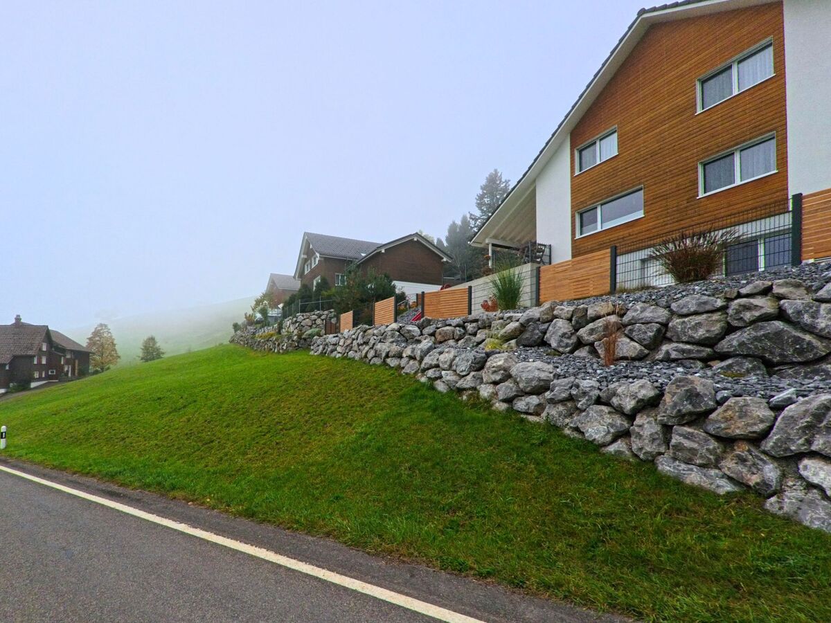 Ein Wohnhaus mit Natursteinmauer liegt leicht erhöht an einer Strasse in Schwellbrunn (9103, Kanton Appenzell Ausserrhoden).