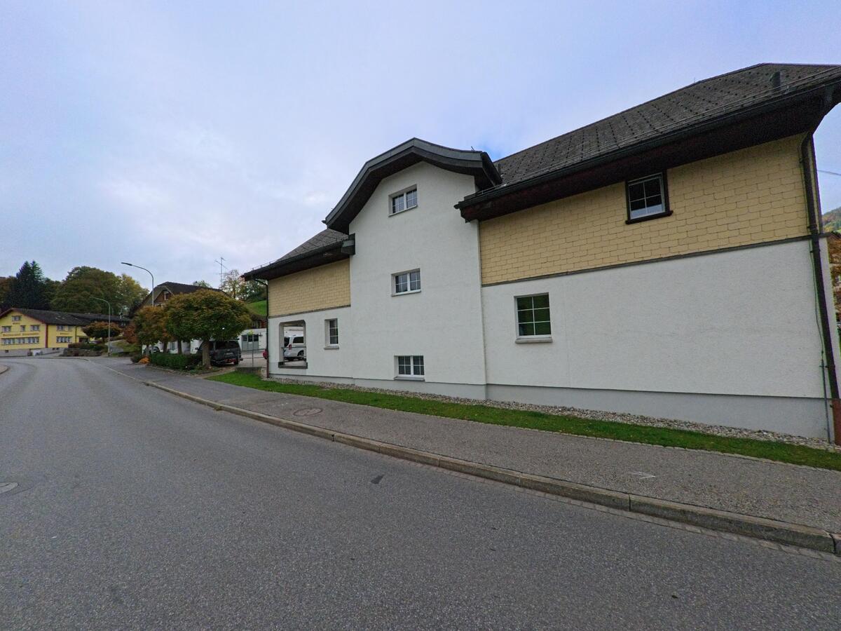 An einer Dorfstrasse in Schwende (9057, Kanton Appenzell Innerrhoden) steht ein grosses helles Gebäude mit gelber Schindelfassade, breitem Dach und angrenzendem Gehweg.  Bildtitel: schwende_9057_gebaeude_mit_gelber_schindelfassade_an_dorfstrasse.