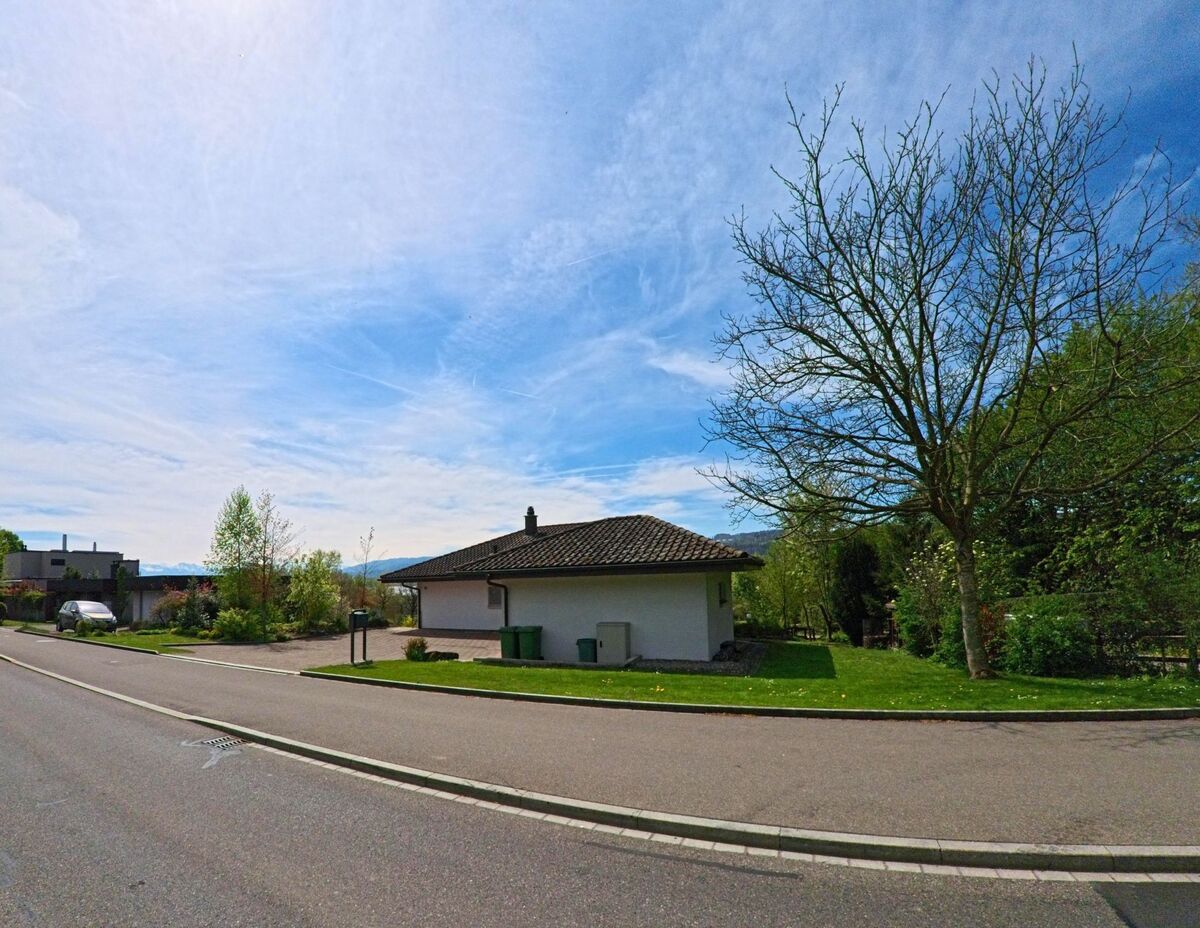 Am Rand von Schwerzenbach (8603 im Kanton Zürich) steht ein eingeschossiges Wohnhaus mit gepflegtem Rasen und kahlem Baum unter leicht bewölktem Himmel.
