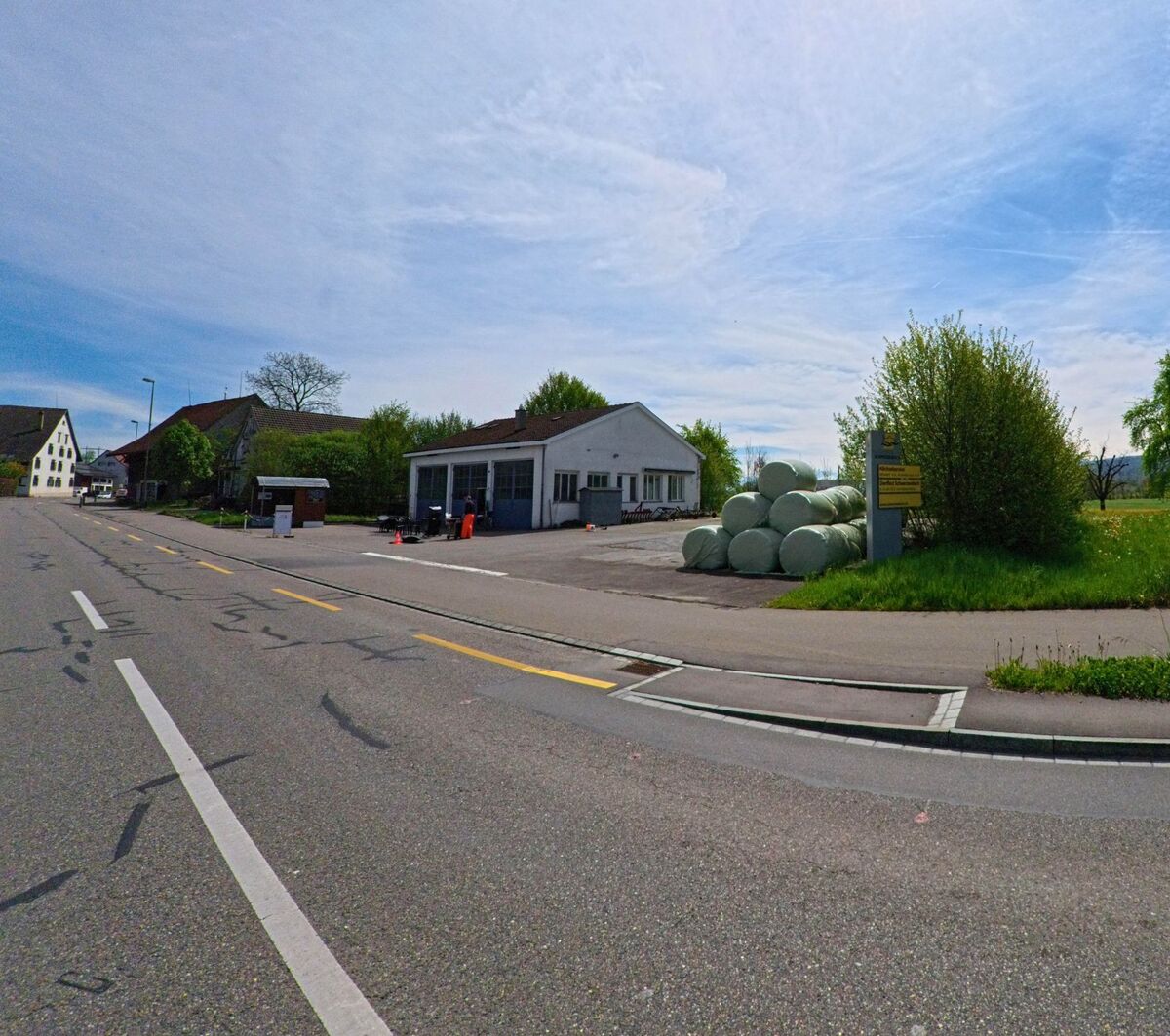 Am Ortsrand von Schwerzenbach (PLZ 8603 im Kanton Zürich) stehen neben einem weissen Werkstattgebäude mehrere grün verpackte Heuballen gestapelt auf dem Asphalt.