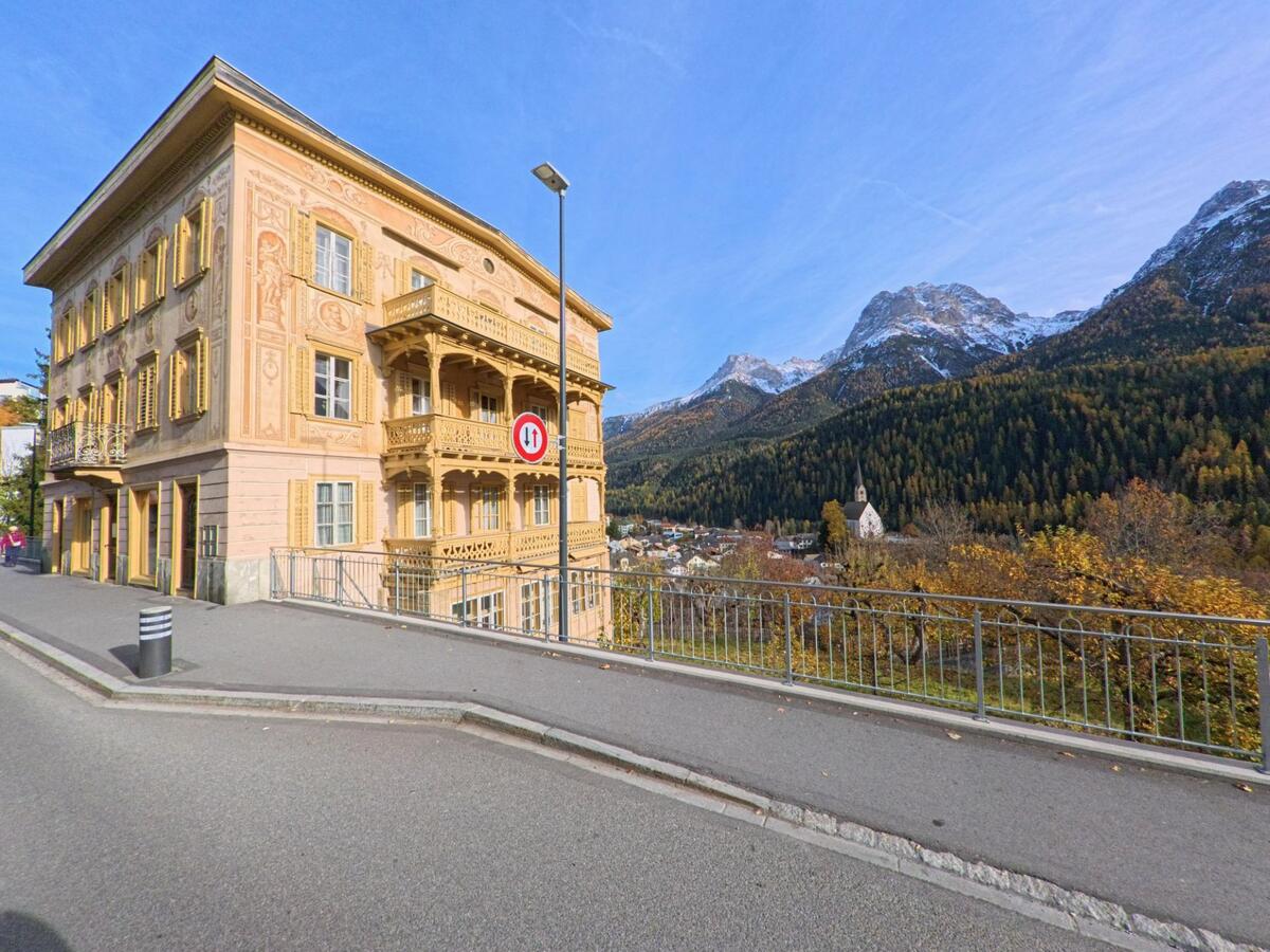 Ein reich verziertes historisches Gebäude steht an einer Strasse in Scuol (7550, Kanton Graubünden), während sich im Hintergrund das herbstliche Bergtal öffnet.