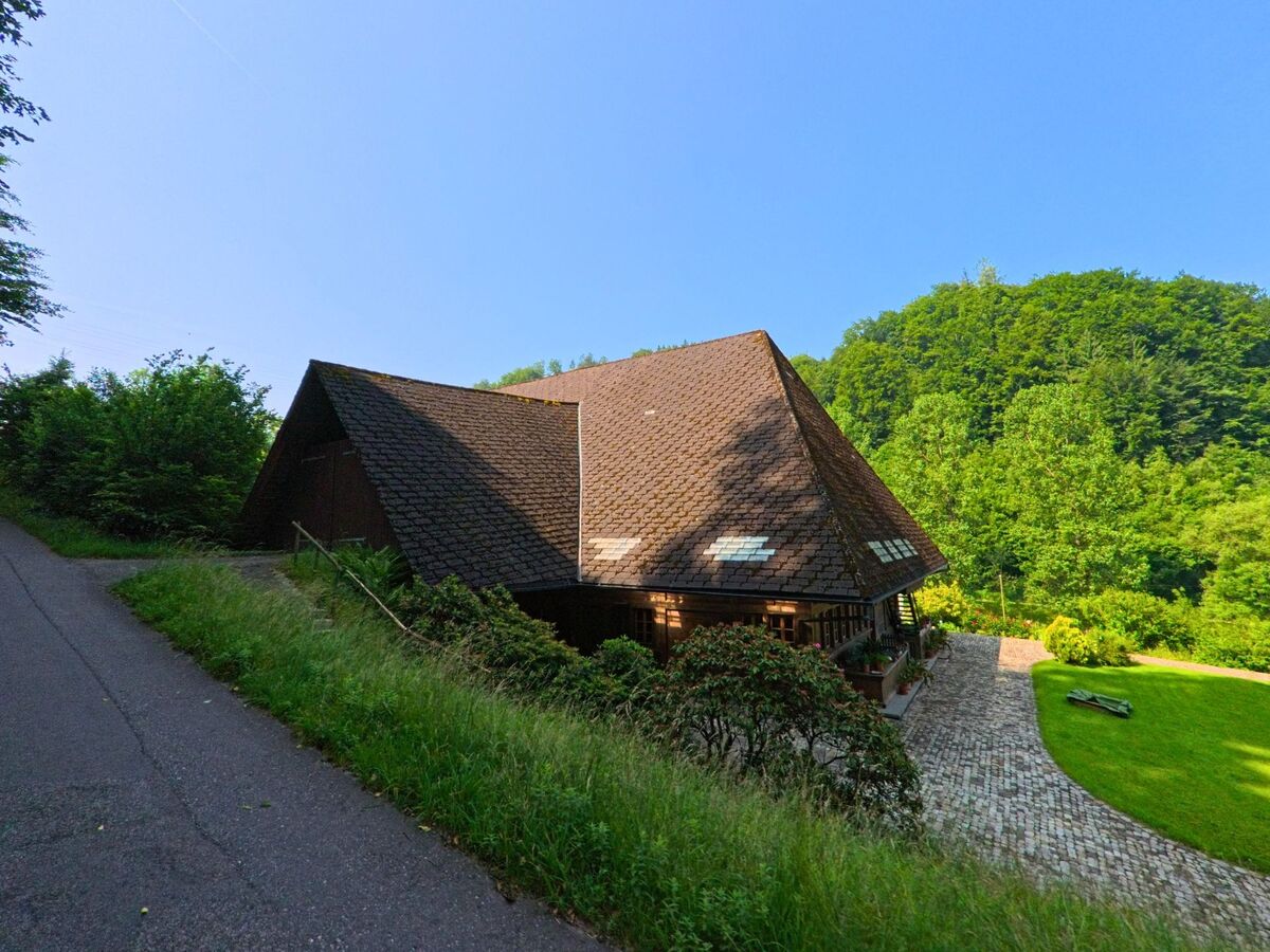 In Seeberg (3475, Kanton Bern) liegt ein Holzhaus mit markantem Walmdach eingebettet in eine grüne Waldlandschaft.