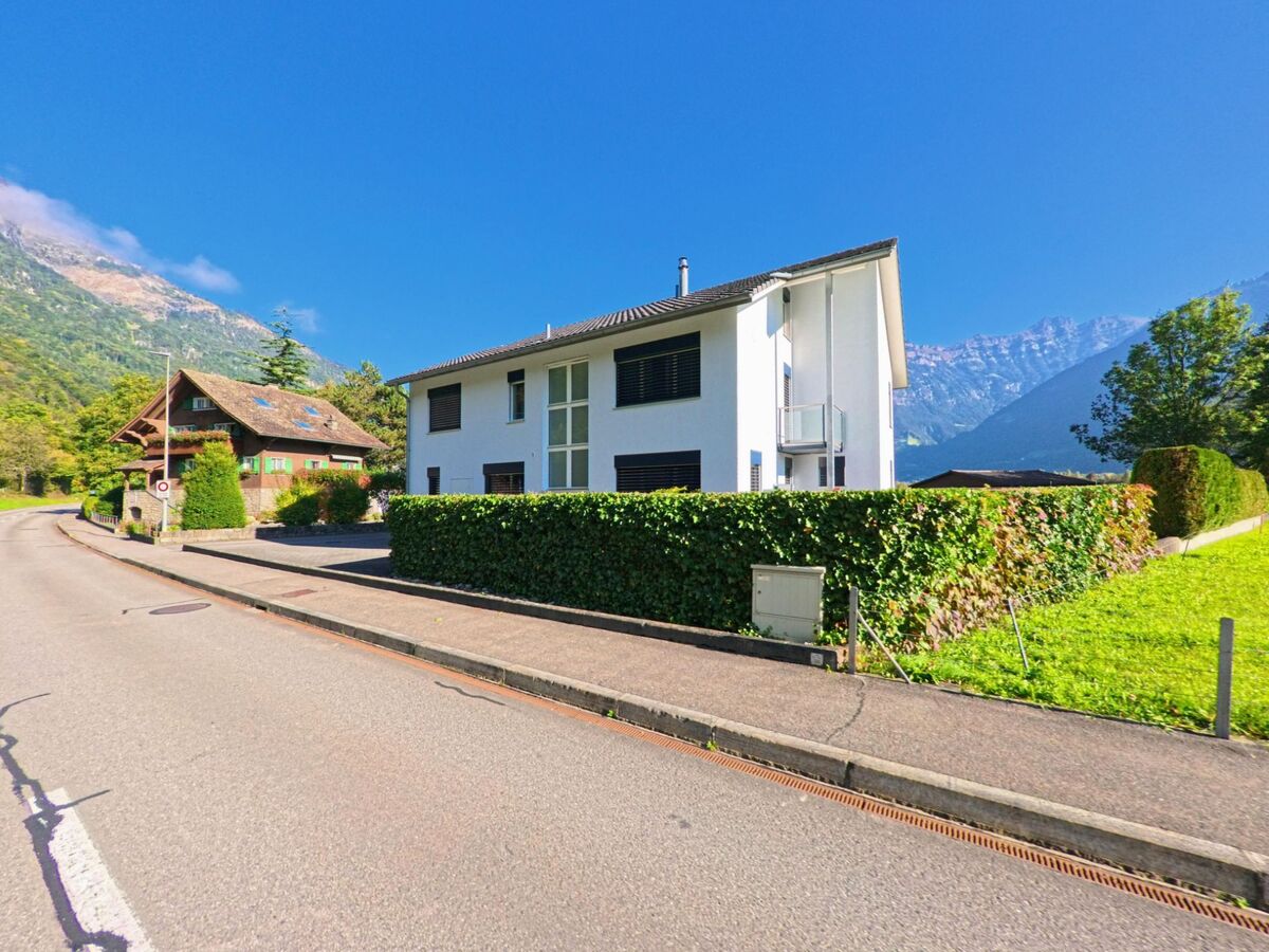 Neben einer ruhigen Strasse mit Gehweg steht ein modernes Wohnhaus in Seedorf (6462, Kanton Uri), umgeben von Hecken und freier Sicht auf die umliegenden Berge.