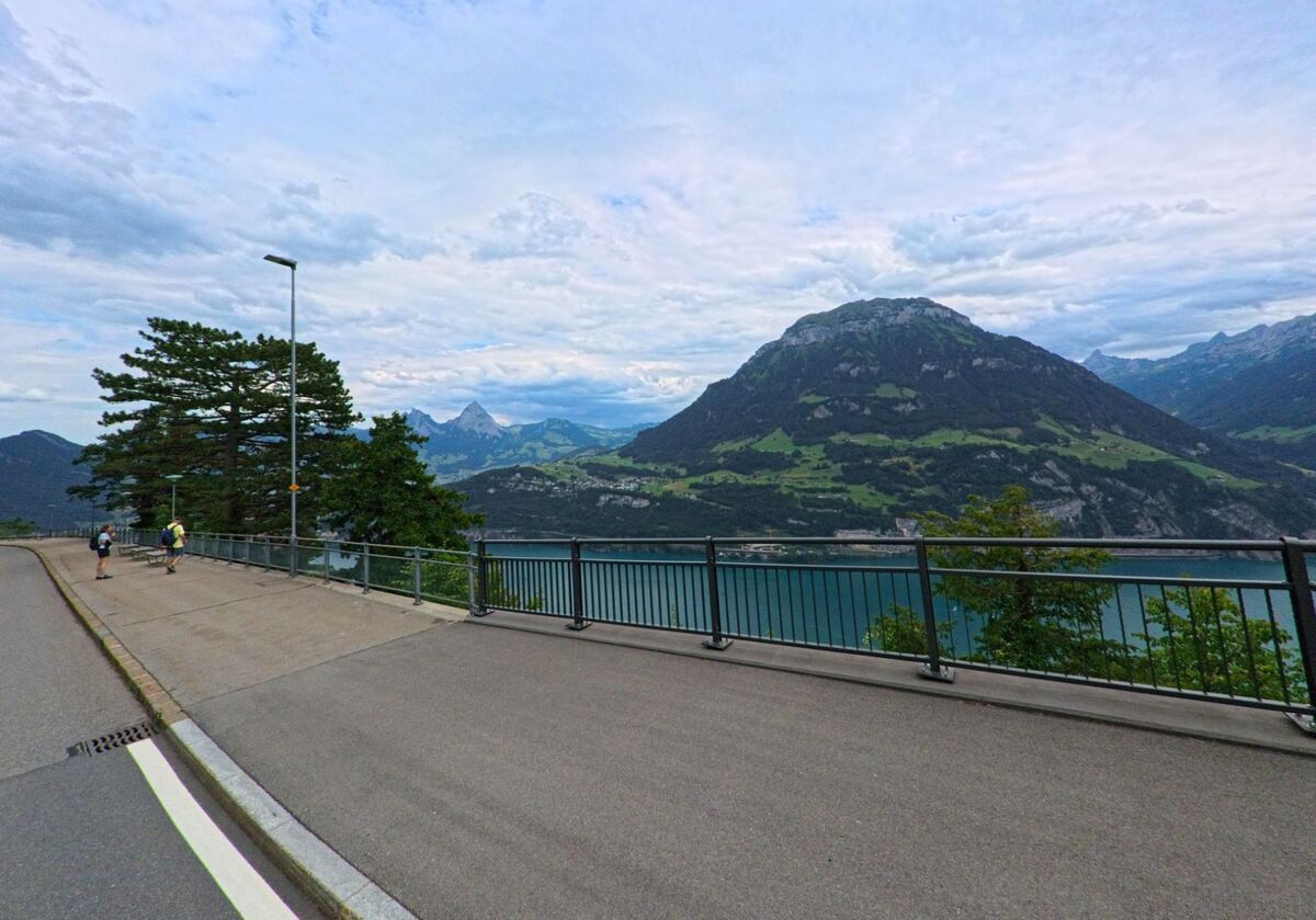 Ein Aussichtspunkt in Seelisberg (6441, Kanton Uri) bietet weiten Blick ueber den Vierwaldstaettersee und die umliegenden Berge mit Wandernden am Strassenrand.