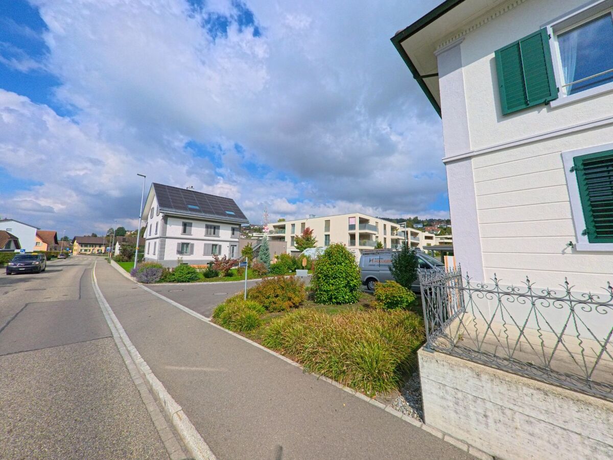 In einem Wohnquartier von Seengen (5707, Kanton Aargau) stehen moderne Mehrfamilienhaeuser und ein renoviertes Einfamilienhaus mit Solardach entlang einer ruhigen Strasse.