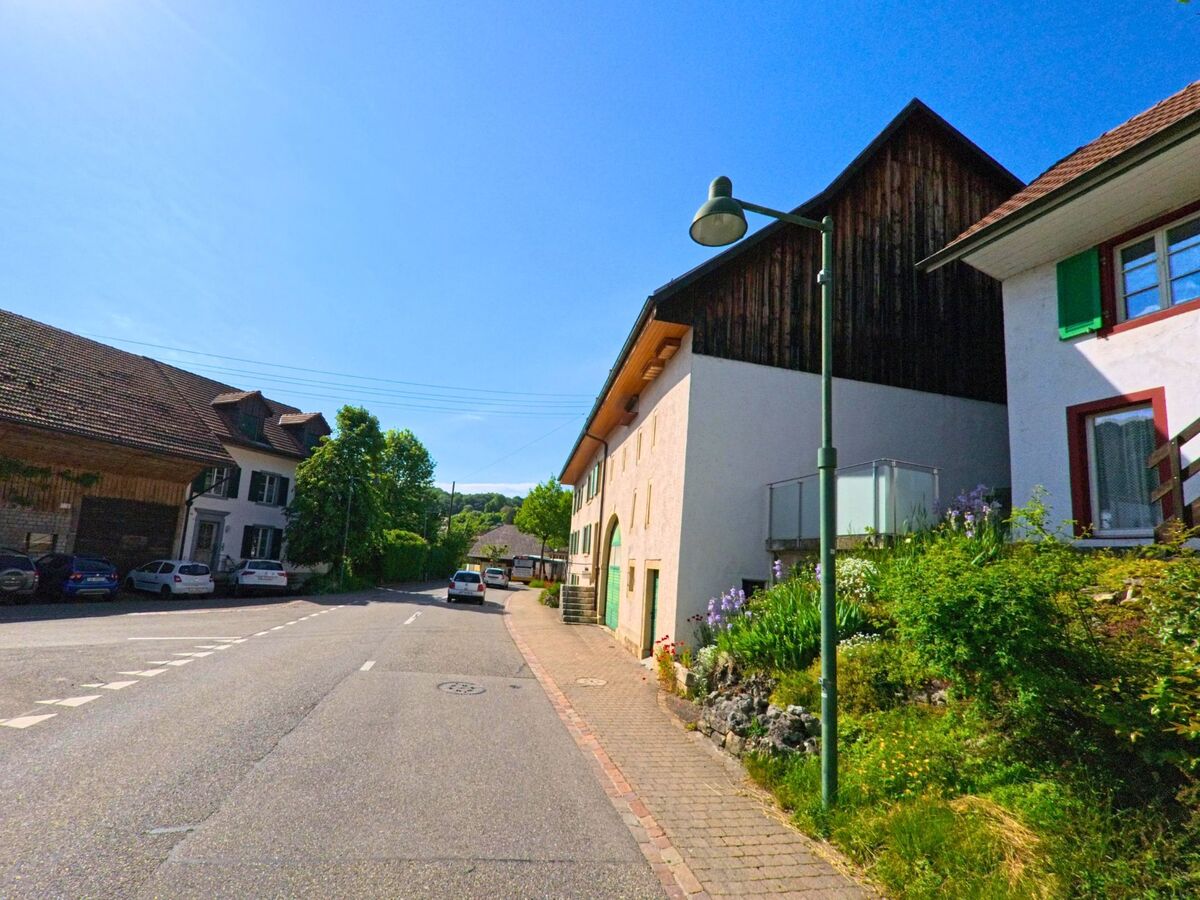 In Seewen (4206, Kanton Solothurn) führt eine sonnige Straße an historischen Häusern entlang, deren Fenster mit grünen Fensterläden verziert sind.