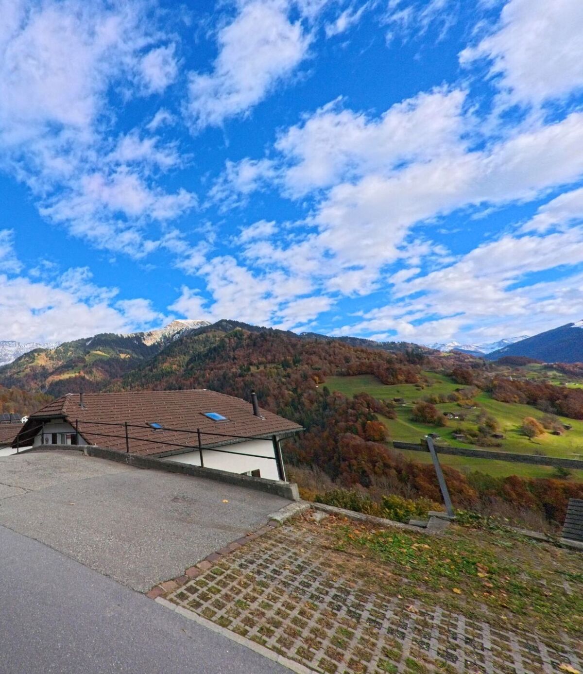 Von einem erhöhten Standort aus eröffnet sich der Blick über die hügelige Landschaft von Seewis im Prättigau (7212, Kanton Graubünden) mit verstreuten Wiesen, Waldflächen und herbstlich gefärbten Berghängen.