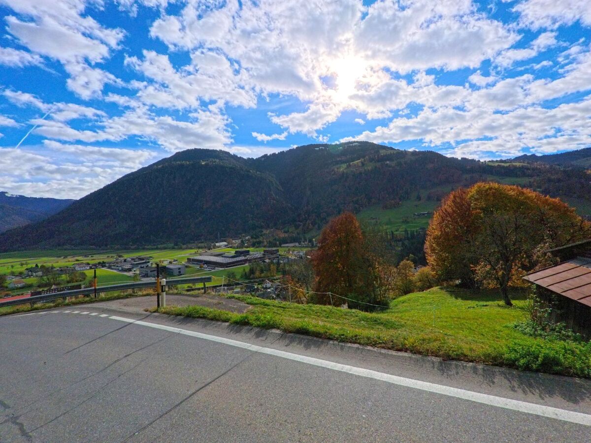 Von einer leicht erhöhten Strasse aus fällt der Blick über das Tal bei Seewis im Prättigau (7212, Kanton Graubünden) mit Gewerbebauten, Wiesen und bewaldeten Hängen unter einer aufgelockerten Wolkendecke.
