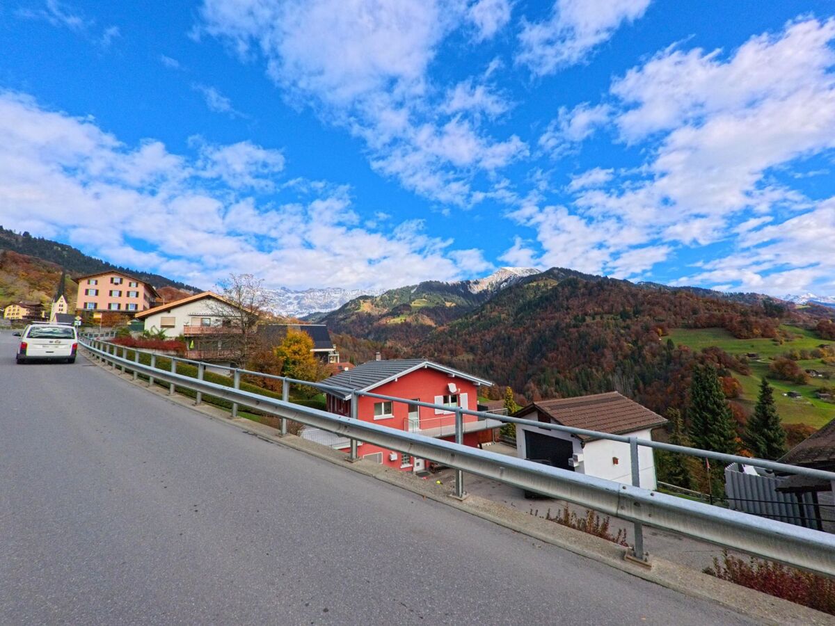Entlang einer leicht erhöhten Strasse zeigt sich ein Wohnquartier in Seewis im Prättigau (7212, Kanton Graubünden) mit Blick über herbstliche Hänge und die Berglandschaft im Hintergrund.