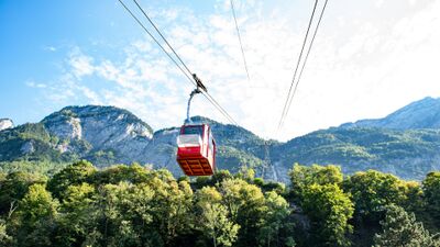 Die Seilbahn-Palfries in Heiligkreuz (8888, Kanton St. Gallen) faehrt mit einer roten Gondel ueber bewaldete Haenge und bietet einen Blick auf die Bergkulisse.