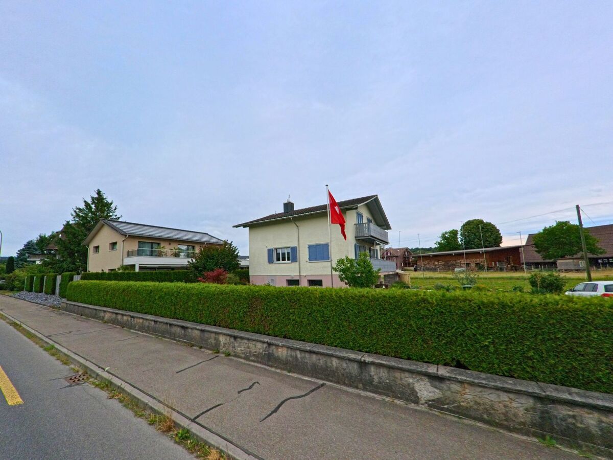 In einem Wohnquartier von Sempach (6204, Kanton Luzern) weht eine Schweizer Fahne vor einem freistehenden Einfamilienhaus mit gepflegter Hecke.