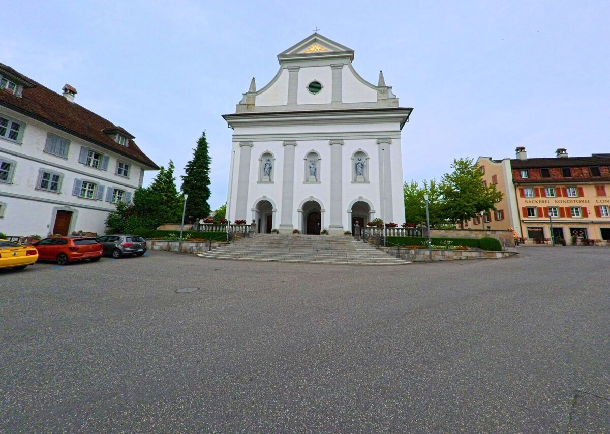 Die eindrucksvolle Fassade der Kirche von Sempach (6204, Kanton Luzern) erhebt sich mit drei Heiligenfiguren über einer breiten Treppe, flankiert von historischen Gebäuden.
