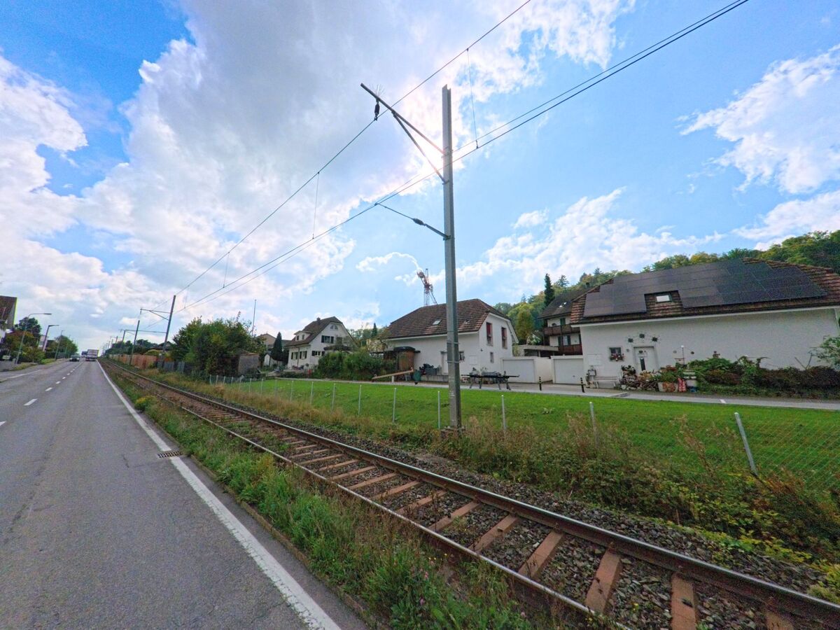 Entlang der Bahnlinie in Seon (5703, Kanton Aargau) stehen Wohnhaeuser mit Solardach neben einer ruhig verlaufenden Landstrasse.