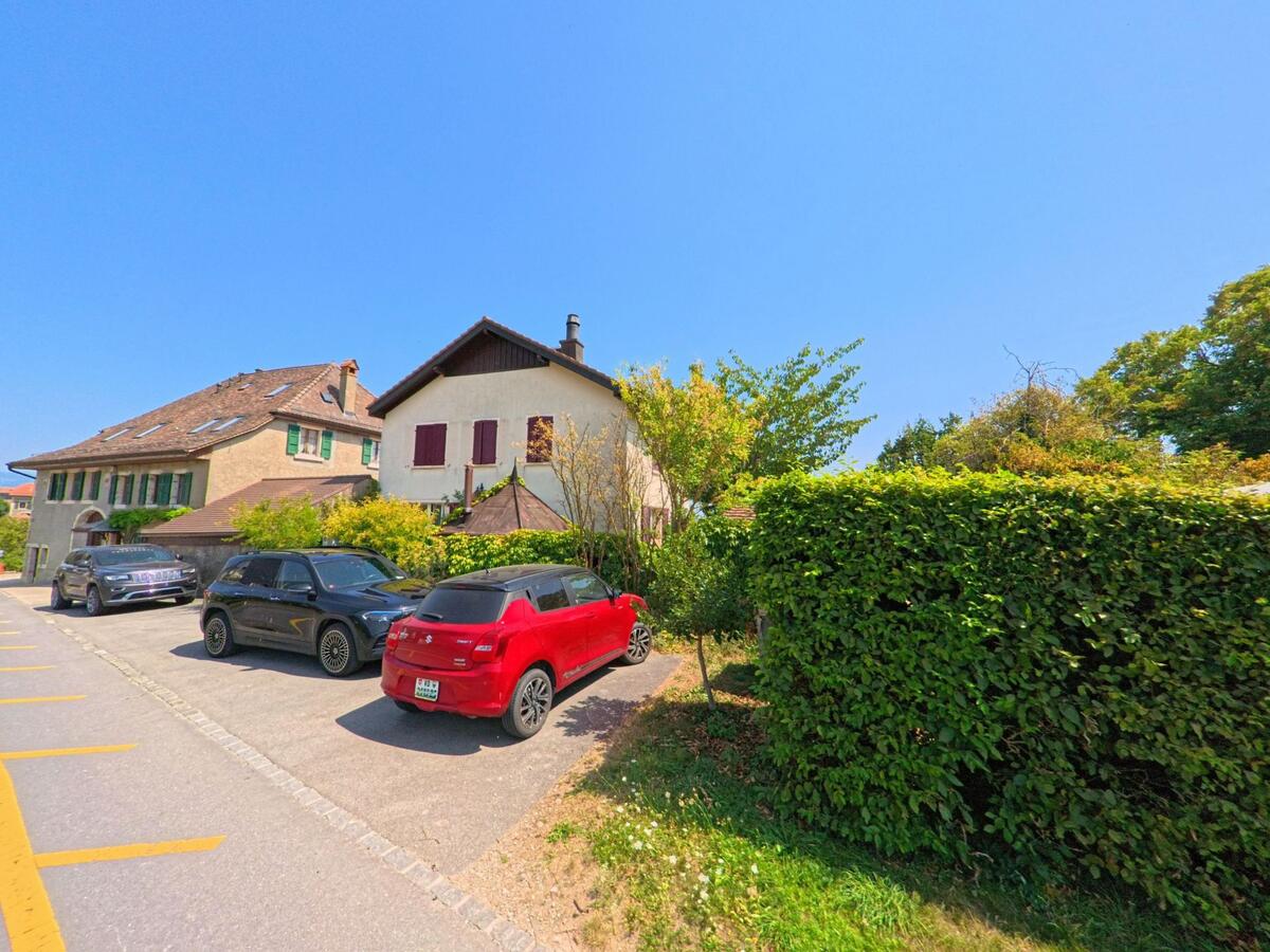 Mehrere geparkte Autos stehen vor traditionellen Wohnhaeusern mit Fensterlaeden in Sergey (1355, Kanton Waadt).