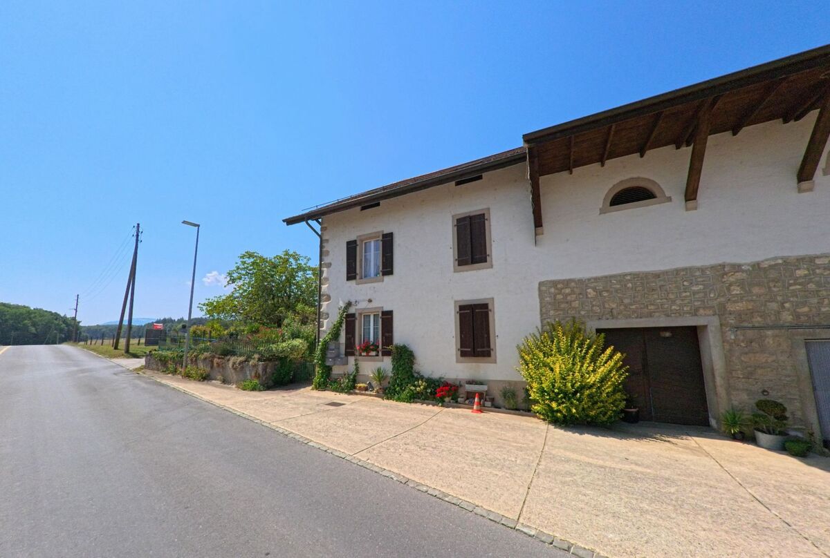 Ein traditionelles Wohnhaus mit Steinmauer und Blumenschmuck steht an der Hauptstrasse in Sergey (1355, Kanton Waadt).