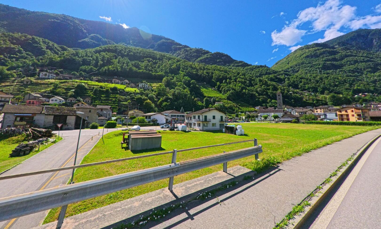 Die Ortschaft Serravalle (6713, Kanton Tessin) liegt eingebettet zwischen gruene Haenge und Weinreben, mit Wohnhaeusern und dem Kirchturm im Zentrum.