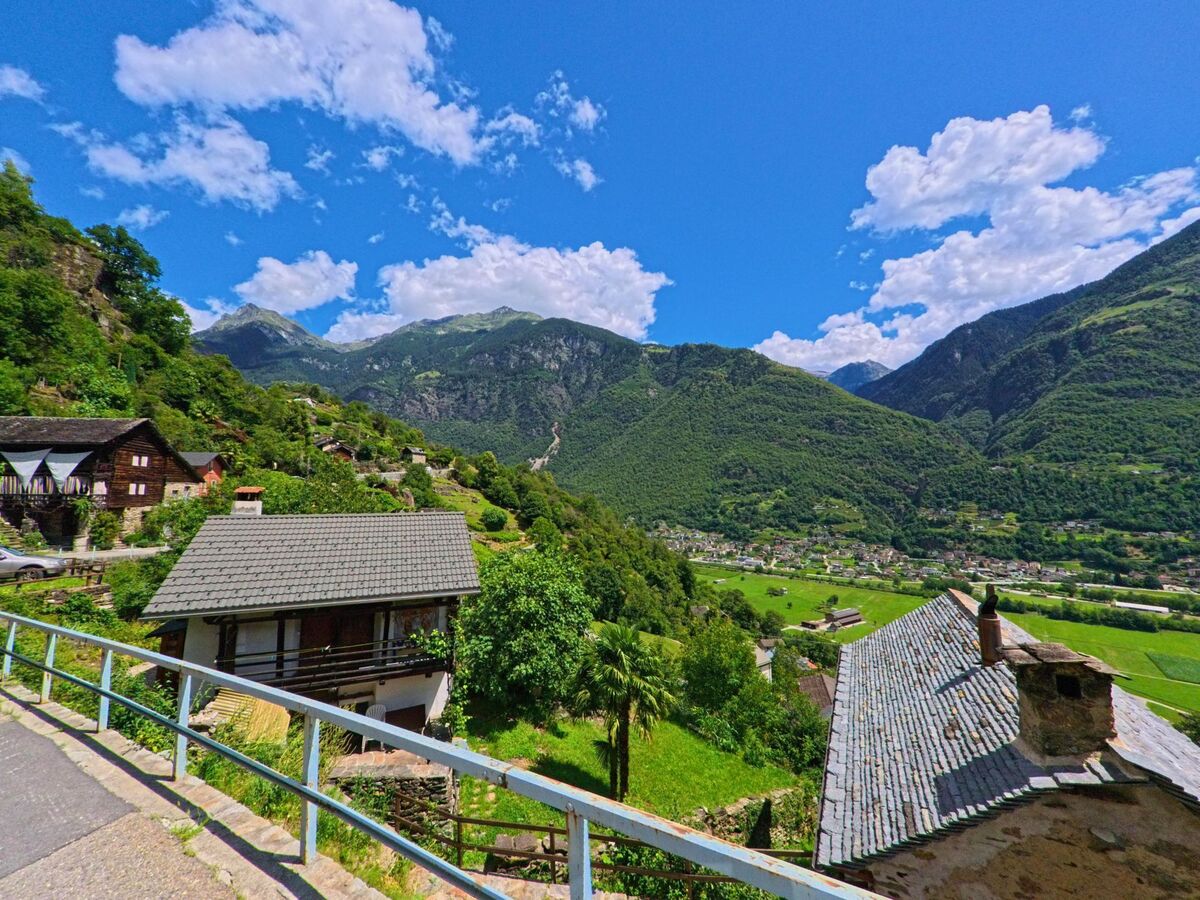 Von einer Strasse in Serravalle (6714, Kanton Tessin) bietet sich ein weiter Blick ueber Hauser mit Steindachern und das gruen umgebene Tal.