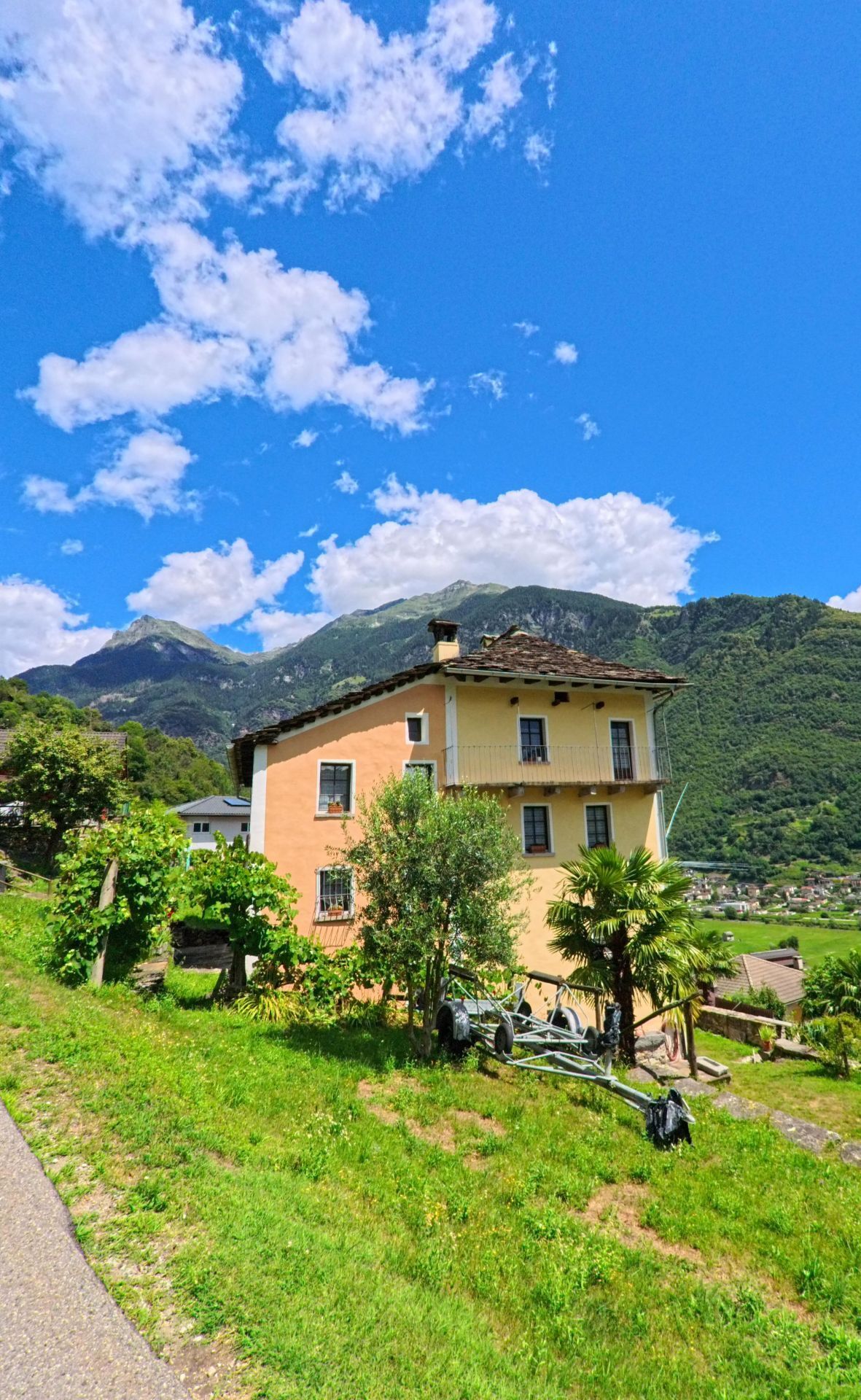 Ein gelbes Wohnhaus in Serravalle (6714, Kanton Tessin) steht am Hang mit Blick auf das Tal und die umliegenden Berge unter blauem Himmel.