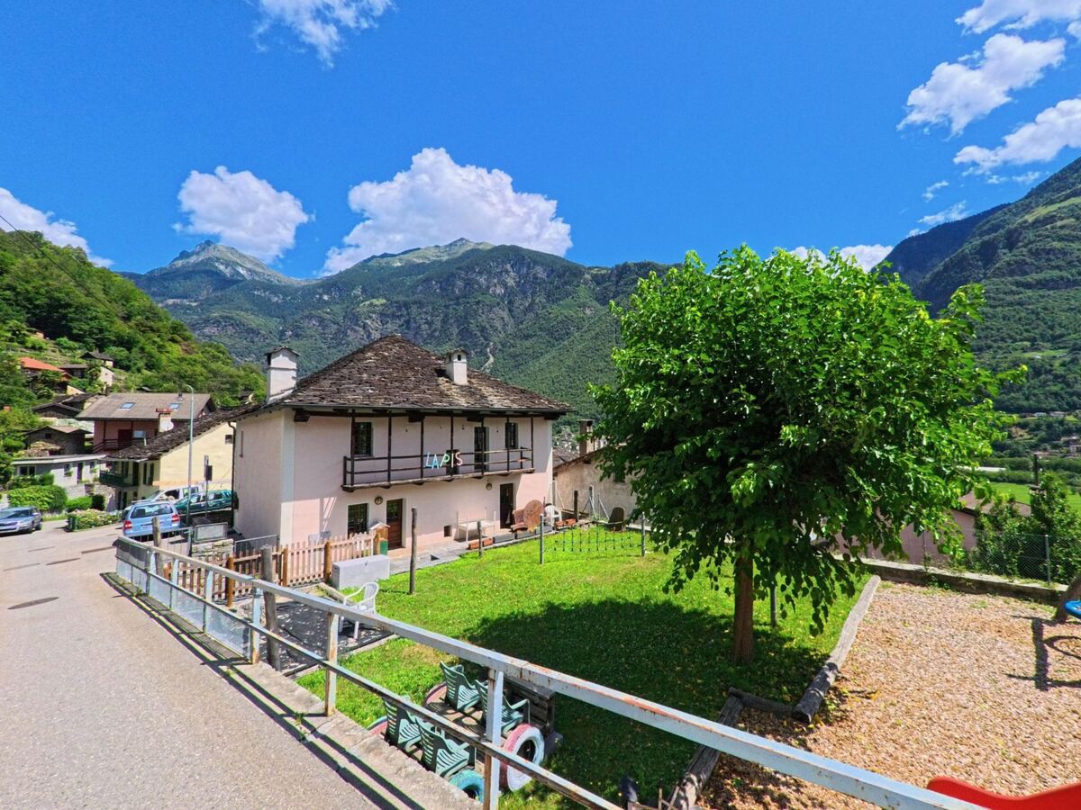 Ein Haus mit typischem Steindach und Garten steht in Serravalle (6714, Kanton Tessin) vor einer beeindruckenden Berglandschaft unter blauem Himmel.