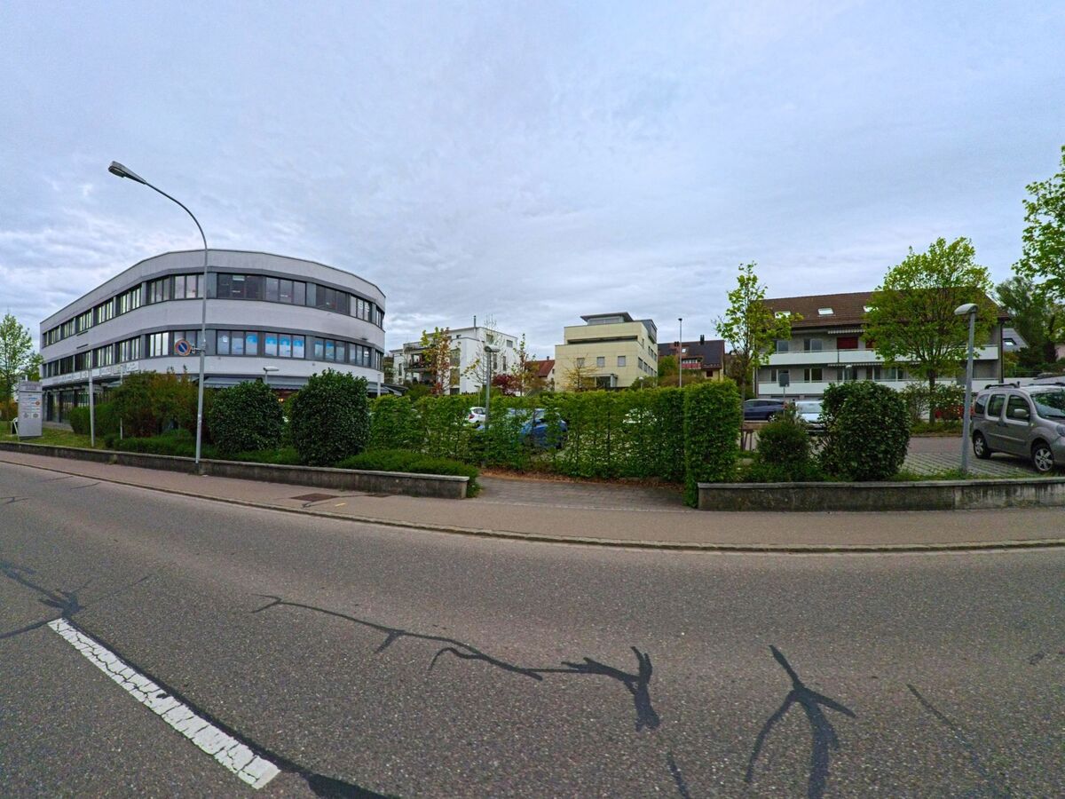 Ein modernes Bürogebäude mit grossen Fenstern steht in Seuzach (8472, Kanton Zürich) an einer Hauptstrasse, gegenüber von Wohnhäusern und Parkplätzen