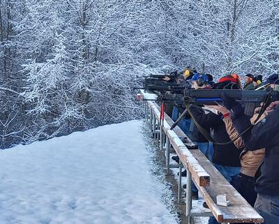 Schuetzinnen und Schuetzen am Schiessstand in winterlicher Landschaft, konzentriertes Zielen mit Gewehren, Schnee auf Boden und Baumen, ruhige Trainingsatmosphaere.