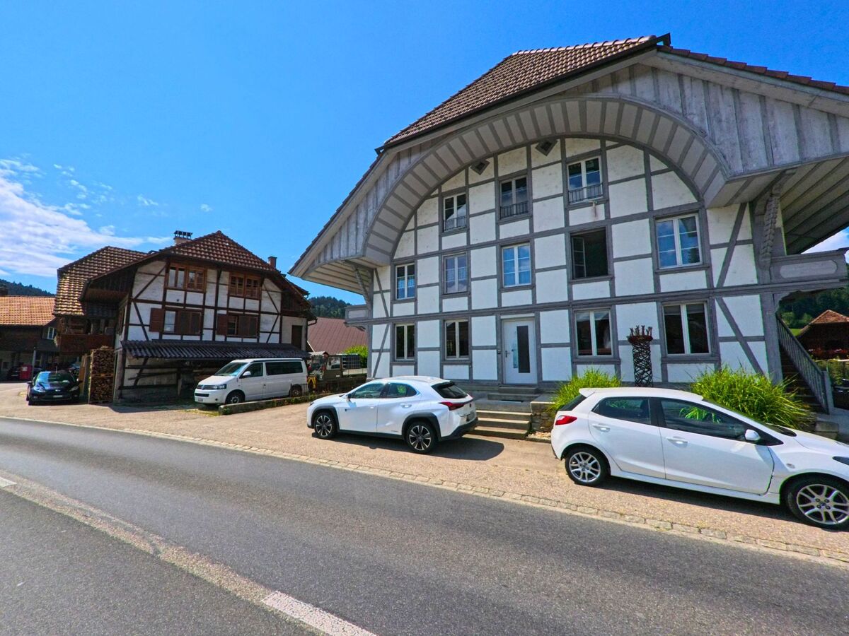 Zwei markante Fachwerkhaeuser in Signau (3535, Kanton Bern) stehen direkt an der Strasse, wobei das vordere durch seine helle Fassade mit grauen Balken hervorsticht.