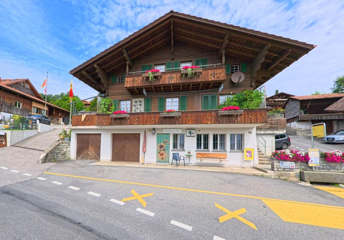 Im Dorfzentrum von Sigriswil (3656, Kanton Bern) steht ein traditionelles Chalet mit Blumenschmuck und einem kleinen Geschaeft, direkt an einer markierten Strassenkreuzung.