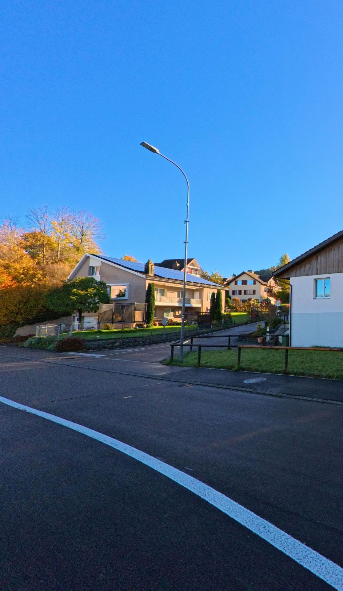 An einer offenen Kreuzung mit Laterne und Wohnhaeusern zeigt sich ein ruhiges Quartier in Sirnach (8371, Kanton Thurgau) bei klarem Himmel und herbstlicher Umgebung.