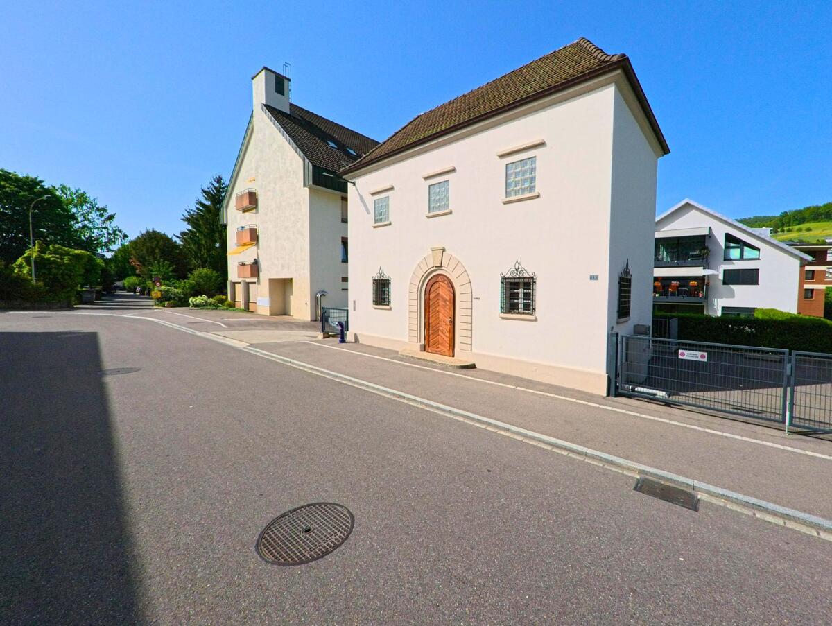 In Sissach (4450, Kanton Baselland) steht ein helles Gebaeude mit auffaelliger Holztuere und vergitterten Fenstern an einer ruhigen Quartierstrasse.