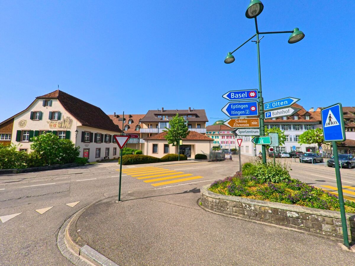 Im Zentrum von Sissach (4450, Kanton Baselland) treffen sich mehrere Strassen an einem Kreisverkehr mit Wegweisern zu Basel, Olten und dem Bahnhof, umgeben von historischen Gebaeuden.