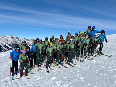 Eine Gruppe von Kindern und Erwachsenen steht mit Skiern auf einer verschneiten Bergpiste in Frutigen (3714, Kanton Bern) und posiert gemeinsam.