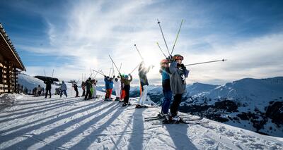 In Rothrist (4852, Kanton Aargau) stehen zahlreiche junge Skifahrer auf einem sonnigen Gipfel und strecken ihre Skistecken in die Hoehe, waehrend sich die Berglandschaft weit im Hintergrund erstreckt.