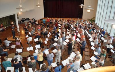 Ein grosses Ensemble aus Chor und Orchester probt gemeinsam in einem Saal in Thun (3600, Kanton Bern) unter der Leitung eines Dirigenten.