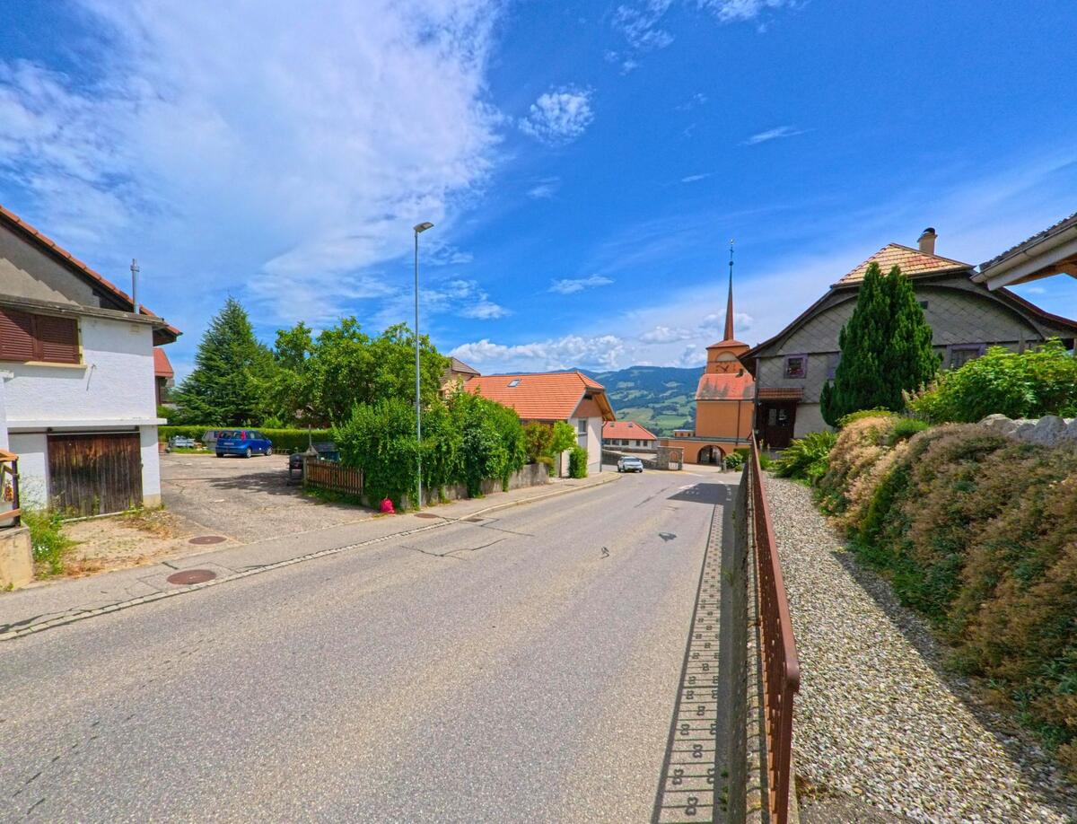 In einer leicht abfallenden Wohnstrasse von Sorens (1643, Kanton Freiburg) ist der Kirchturm mit Uhr weithin sichtbar zwischen den Häusern eingebettet.