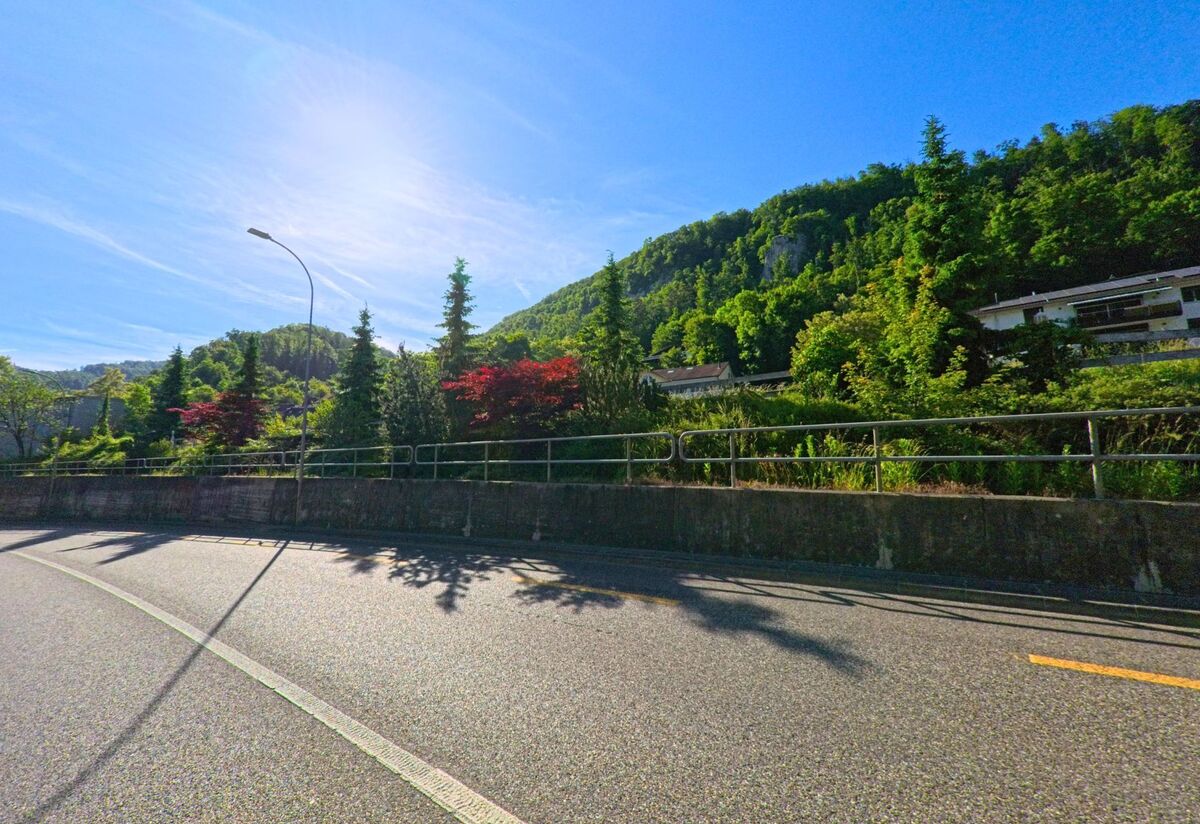 Eine sanft geschwungene Strasse in Soyhières (2805, Kanton Jura) verläuft am Hang entlang, gesäumt von Bäumen und buntem Laub mit Blick auf bewaldete Höhenzüge.