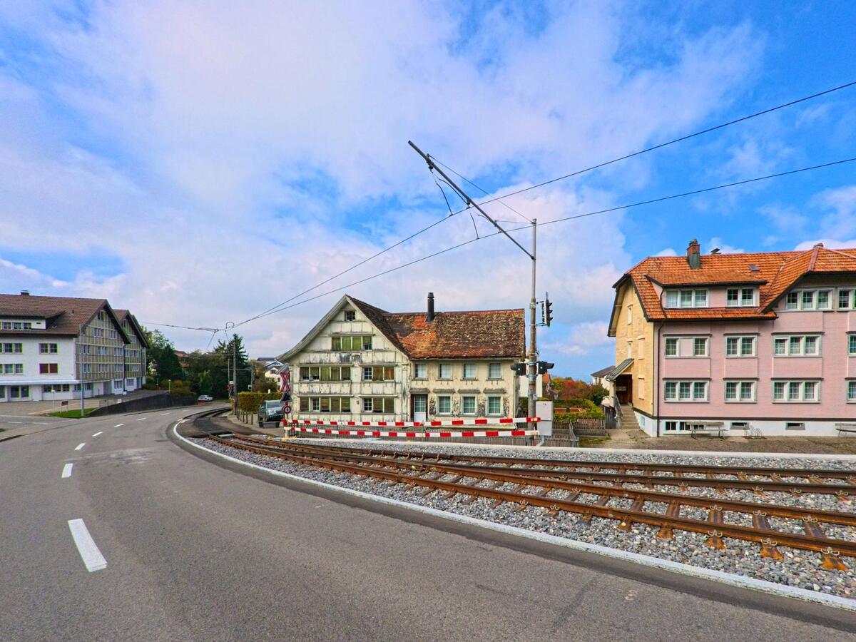 Die Bahnlinie verläuft parallel zur Kurve einer Strasse mit Wohnhäusern in Speicher (9037, Kanton Appenzell Ausserrhoden).