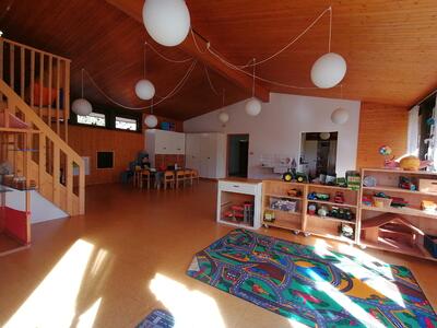 Der helle Spielraum in Konolfingen 3510 im Kanton Bern zeigt unter einer Holzdecke Spielteppich, Fahrzeuge, Regale und kindgerechte Tische.