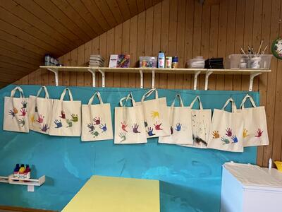In der Spielgruppe Zwärgli Oberdorf aus Oberdorf (6370, Kanton Nidwalden) hängen bemalte Stofftaschen mit bunten Handabdrücken im Bastelraum an einer Leine.