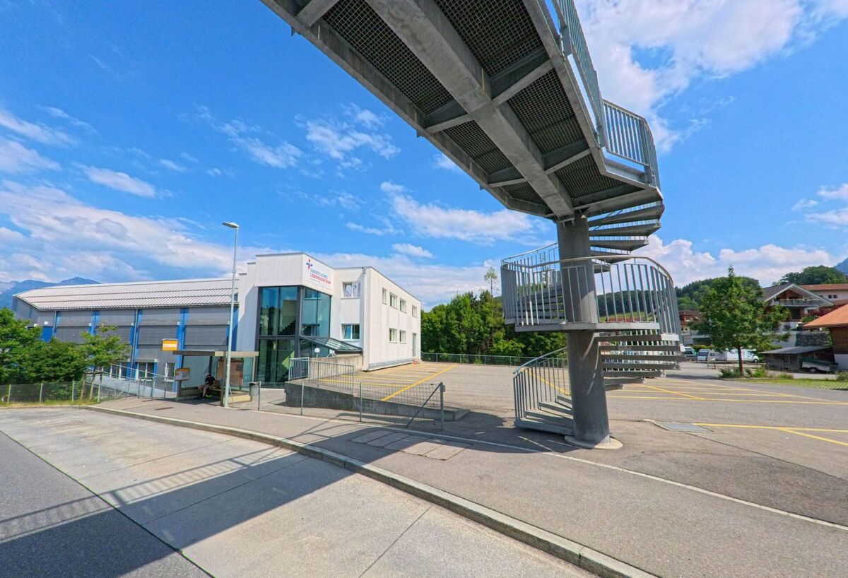 In Spiez (3700, Kanton Bern) verbindet eine Wendeltreppe aus Metall eine Fussgängerüberführung mit dem Gelände der Oberstufenschule, das von Schulgebäuden und Sporthalle geprägt ist.