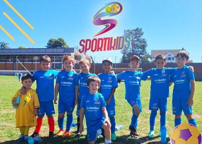 Auf einem Rasenplatz in Dübendorf (8600, Kanton Zürich) stehen mehrere Kinder in blauen Sporttrikots unter dem Sportikids-Logo.