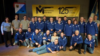 In Meilen (8706, Kanton Zuerich) posiert die Gruppe der Sportschuetzen Feld-Meilen in blauen Vereinsjacken vor Bannern, die auf ihr Jubilaeum hinweisen.
