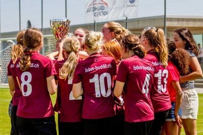 Eine Jugendmannschaft aus Kaufdorf (3126, Kanton Bern) steht auf dem Fussballplatz zusammen und haelt nach einem Spiel einen Pokal in die Hoehe.
