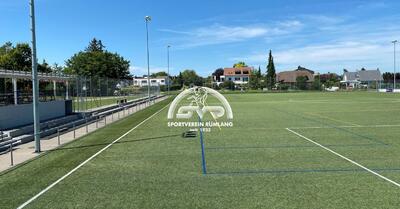 In Ruemlang (8153, Kanton Zuerich) zeigt das Bild das grosszuegige Fussballfeld des Sportvereins Ruemlang bei sonnigem Wetter, mit Blick auf die umliegenden Wohnhaeuser.