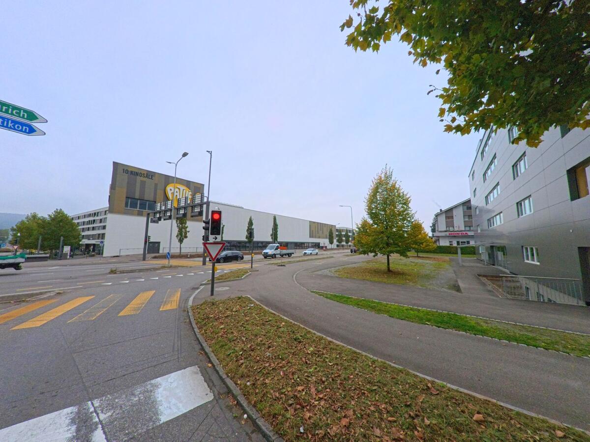 In Spreitenbach (8957, Kanton Aargau) liegt eine vielbefahrene Kreuzung mit Fussgaengerstreifen vor dem grossen Kino- und Freizeitgebaeude Pathé, flankiert von modernen Wohn- und Gewerbebauten.