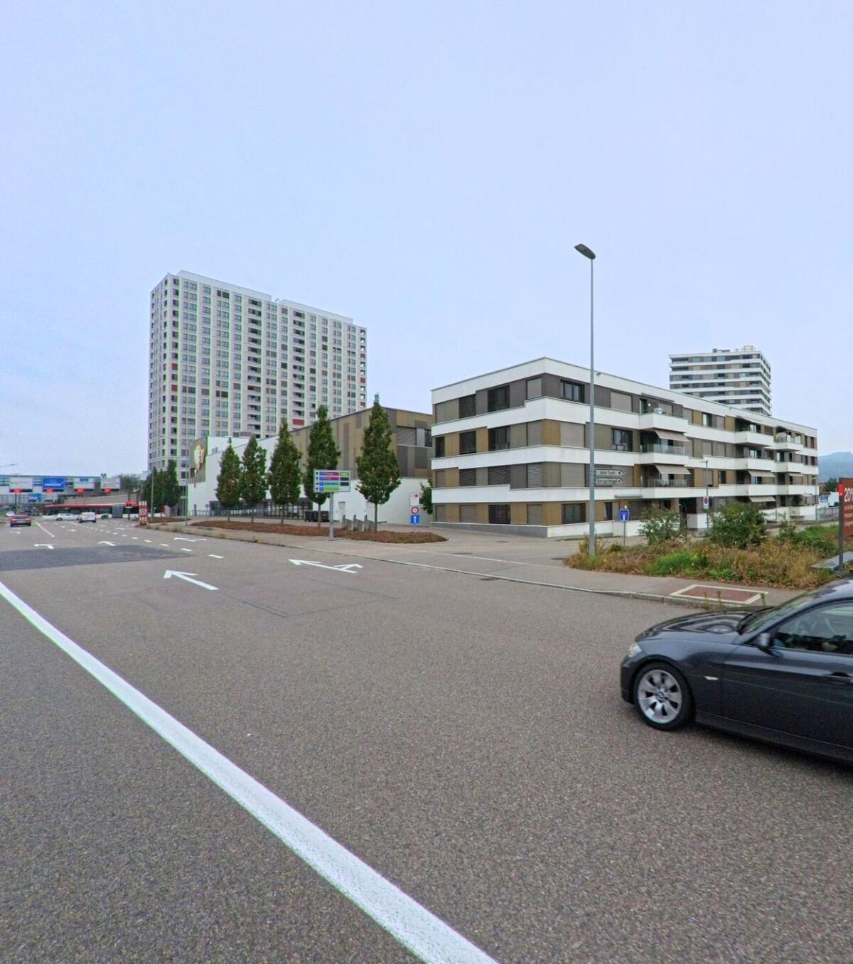 In Spreitenbach (8957, Kanton Aargau) praegen moderne Wohnbauten und ein hohes Hochhaus das Bild einer breiten Verkehrsschneise, die in Richtung Einkaufs- und Gewerbegebiet fuehrt.