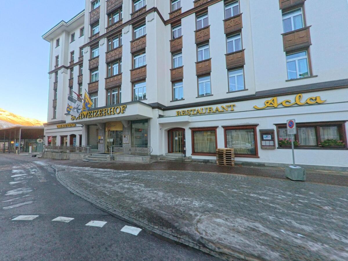Vor einem traditionsreichen Hotel- und Restaurantgebäude mit klassischer Fassade verläuft eine gepflasterte Strasse in St. Moritz (7500, Kanton Graubünden) bei kühlem Morgenlicht.