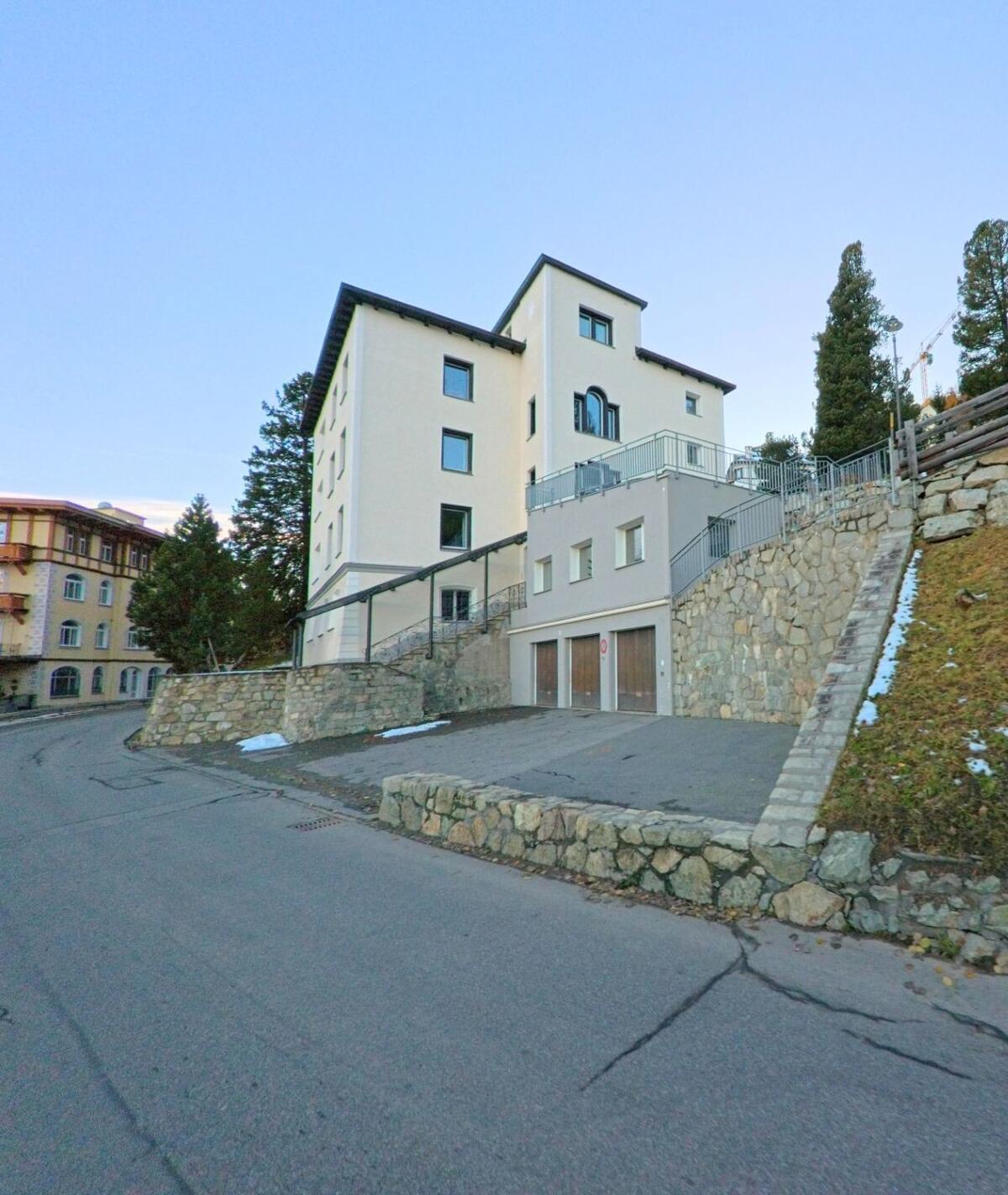 Ein modernes Wohngebäude mit Terrassen und Natursteinmauern steht in St. Moritz (7500, Kanton Graubünden) an einer leicht ansteigenden Quartierstrasse.