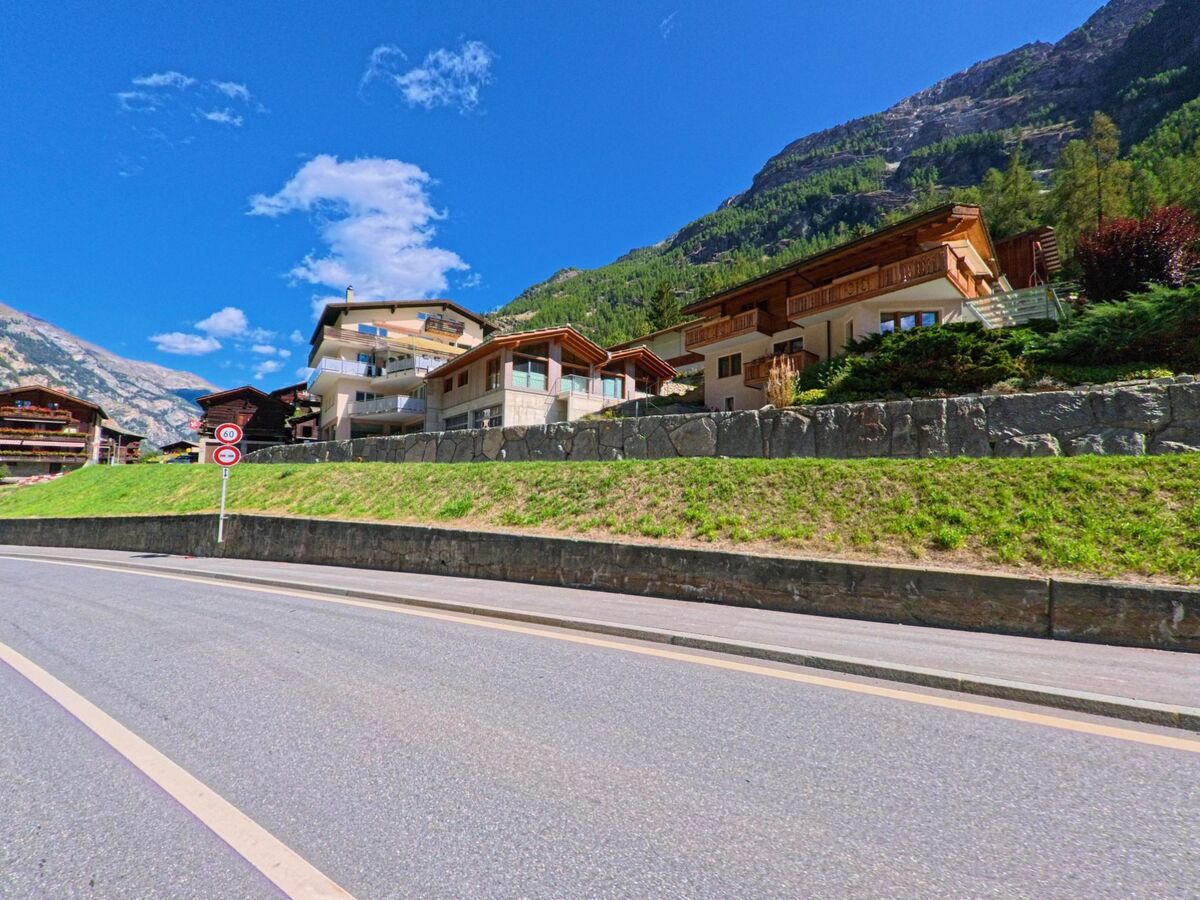 Mehrere moderne Chalets in St. Niklaus (3924, Kanton Wallis) stehen oberhalb einer Strasse am Hang, umgeben von grünen Hängen und Berglandschaft.