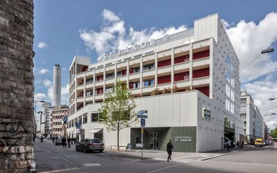 An einer Strassenecke in Zuerich (8005, Kanton Zuerich) steht das moderne Gebaeude der Stiftung St. Jakob mit heller Fassade und roten Balkonen.