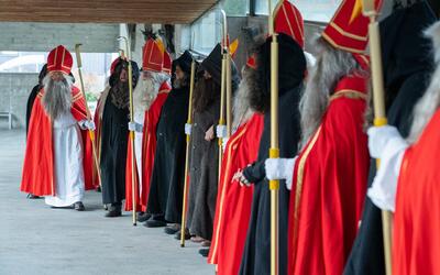 Mitglieder der St. Niklausvereinigung Buchs/Grabs stehen in Buchs/Grabs (9472, Kanton St. Gallen) in roten Nikolausgewändern und dunklen Begleiterkostümen mit Stäben in einer Reihe.